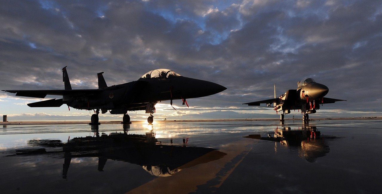 Zwei Kampfjets in der Dämmerung auf nassem Rollfeld, ihre Spiegelung im Wasser