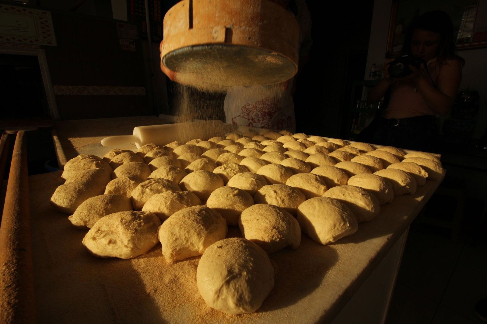 Teiglinge auf einem Bäckereitisch im goldenen Licht, Mehl wird gesiebt
